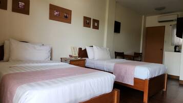 Una habitación de hotel con dos camas, una mesita de noche de madera, una pequeña mesa con sillas y obras de arte colgadas en la pared.