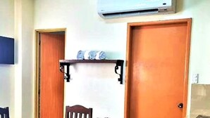 A dining area with a wooden table and chairs, a small shelf with items, and an air conditioning unit above the door. - Balay ni Manuel ken Maria Boutique Hotel (San Fernando)