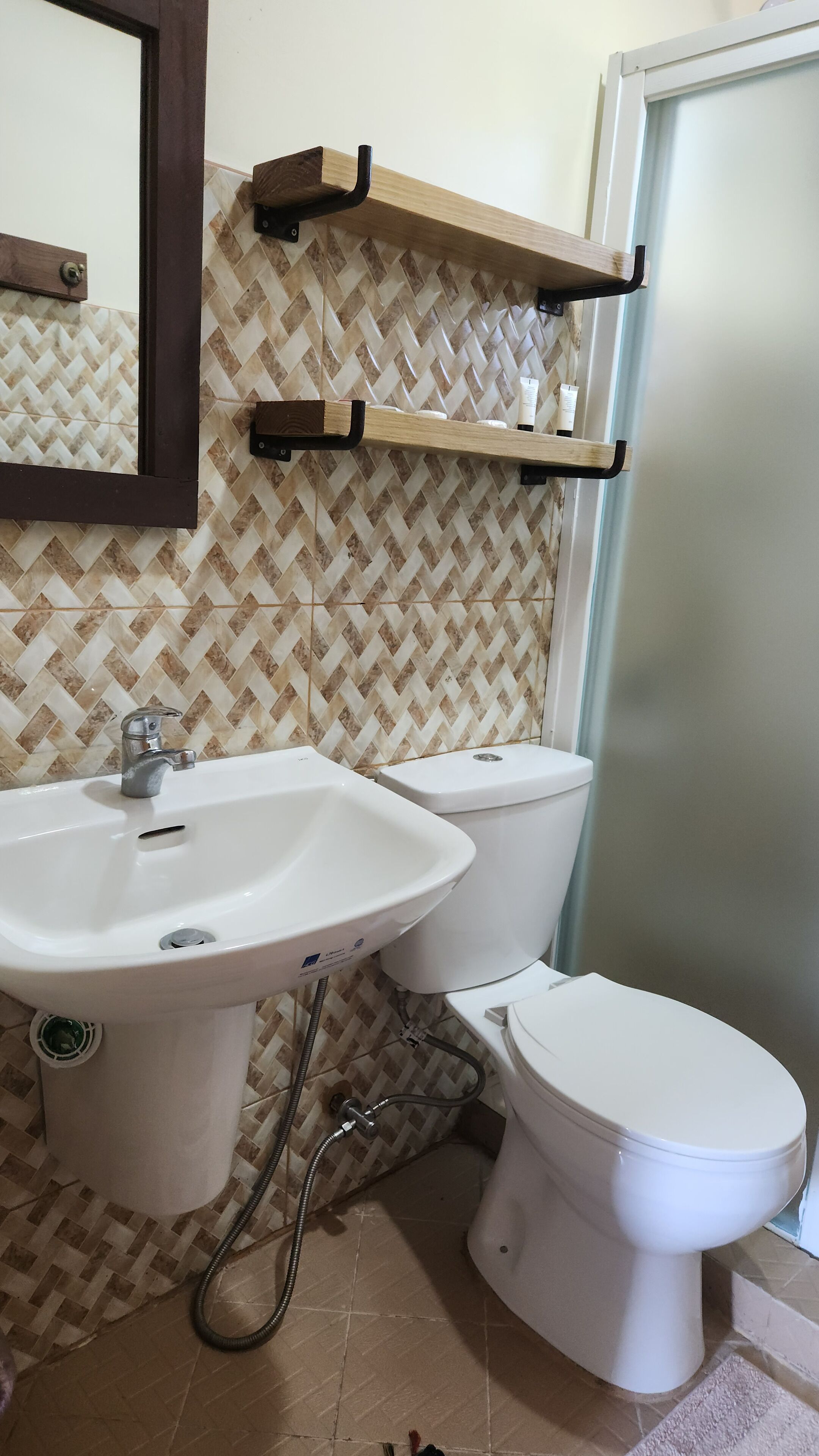 Ein Badezimmer mit einem weißen Waschbecken, zwei Toiletten, einem Spiegel und einem Holzregal über dem Waschbecken.