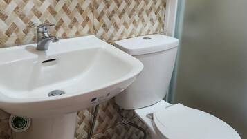 Un bagno con un lavandino bianco, due servizi igienici, uno specchio e una mensola in legno sopra il lavandino.