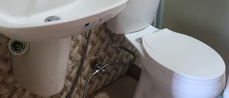 Un baño con un lavabo blanco, dos inodoros, un espejo y un estante de madera sobre el lavabo.
