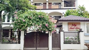 A building with a gated entrance, a sign for 'Baly Restaurant', and a tree with pink flowers. - Balay ni Manuel ken Maria Boutique Hotel (San Fernando)