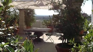 Un espace extérieur aménagé en terrasse, avec une table et des chaises, entouré de plantes en pot et agrémenté d’une pergola offrant de l’ombre.
