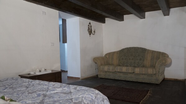 A bedroom with a bed, a sofa, a small table, and a wall-mounted light fixture. - La Querencia (Palermo)
