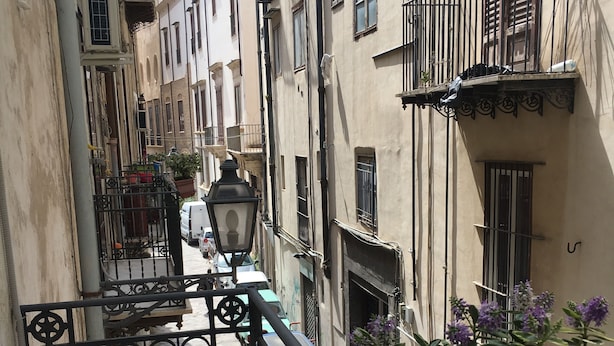 A narrow street with buildings on either side, a metal gate, and potted plants. - La Querencia (Palermo)