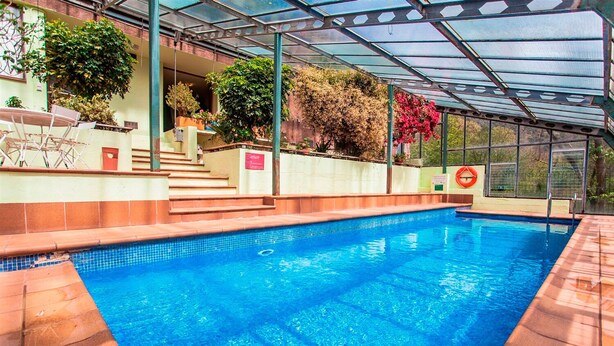 An indoor swimming pool with a glass ceiling, surrounded by steps and potted plants.