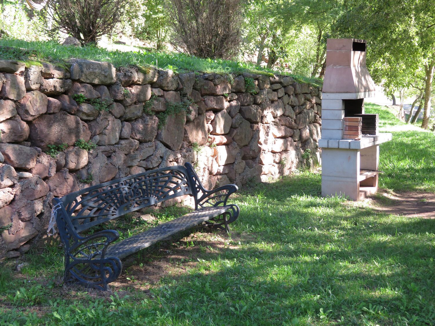 A stone wall, a metal bench, and a brick oven in a park.