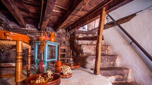A rustic room with a wooden table, a chair, a small blue stool, and a stone staircase.