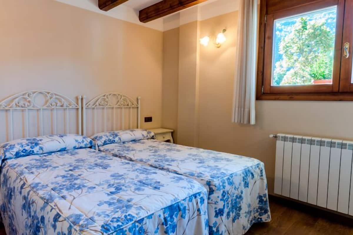 Een slaapkamer met een tweepersoonsbed, een nachtkastje, een raam met gordijnen en een radiator.
