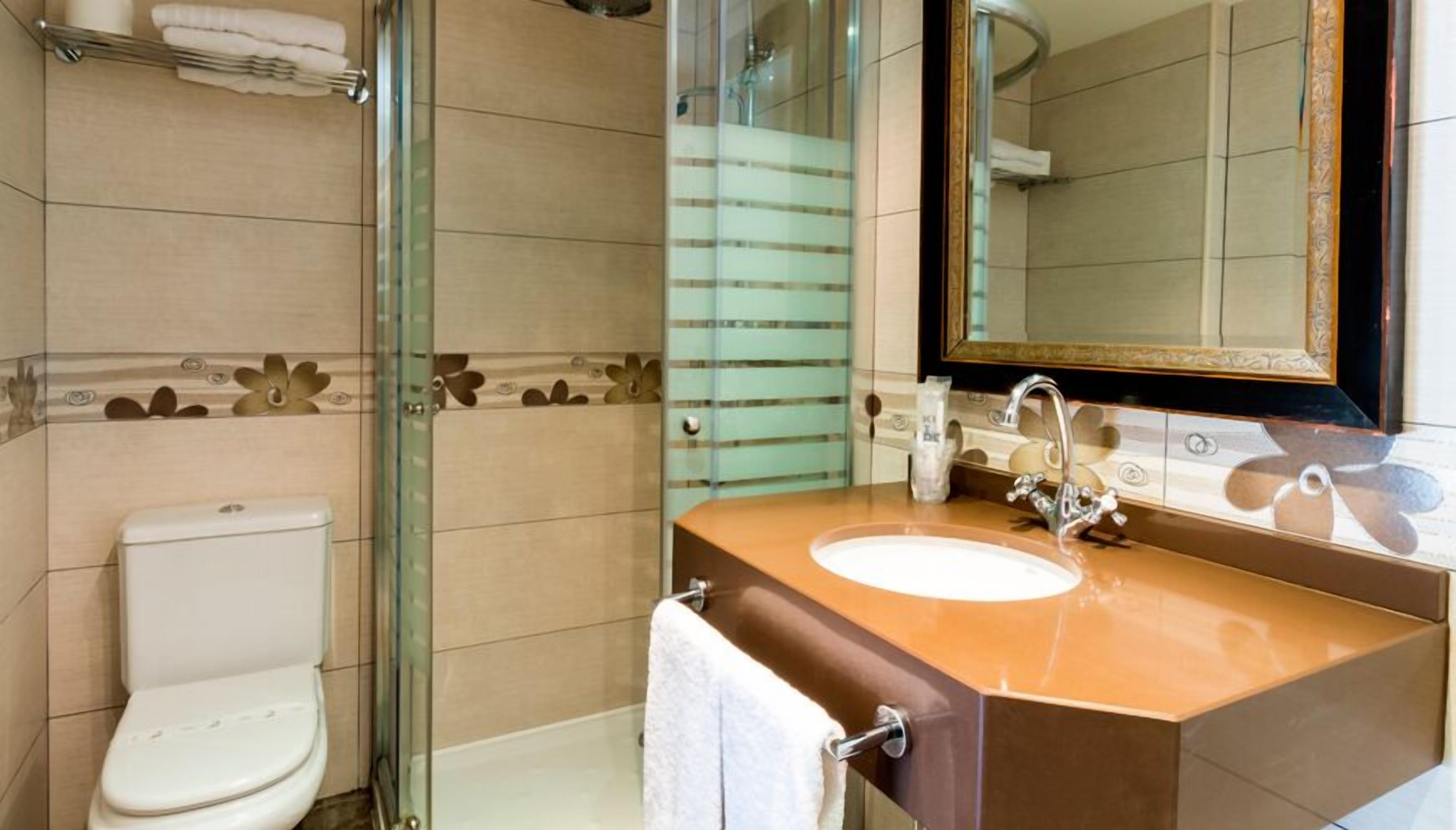 Une salle de bain avec une douche à parois de verre, des toilettes blanches, un meuble-lavabo marron et un grand miroir.