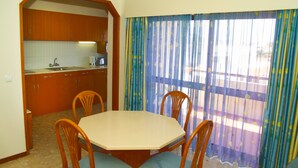 Ein Essbereich mit Tisch und Stühlen, im Hintergrund eine Küche und ein Fenster mit Vorhängen.