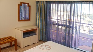 Ein Schlafzimmer mit einem Bett, einem kleinen Schreibtisch, einem Stuhl und einem Fenster mit Vorhängen.