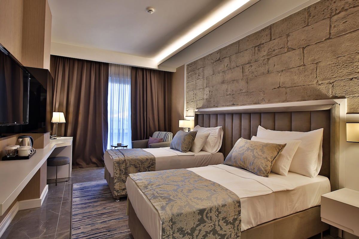 A hotel room with two beds, a desk, a television, and a stone accent wall.