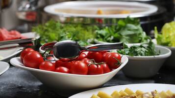 A buffet table with a bowl of tomatoes, a plate of sliced potatoes, and a bowl of greens.