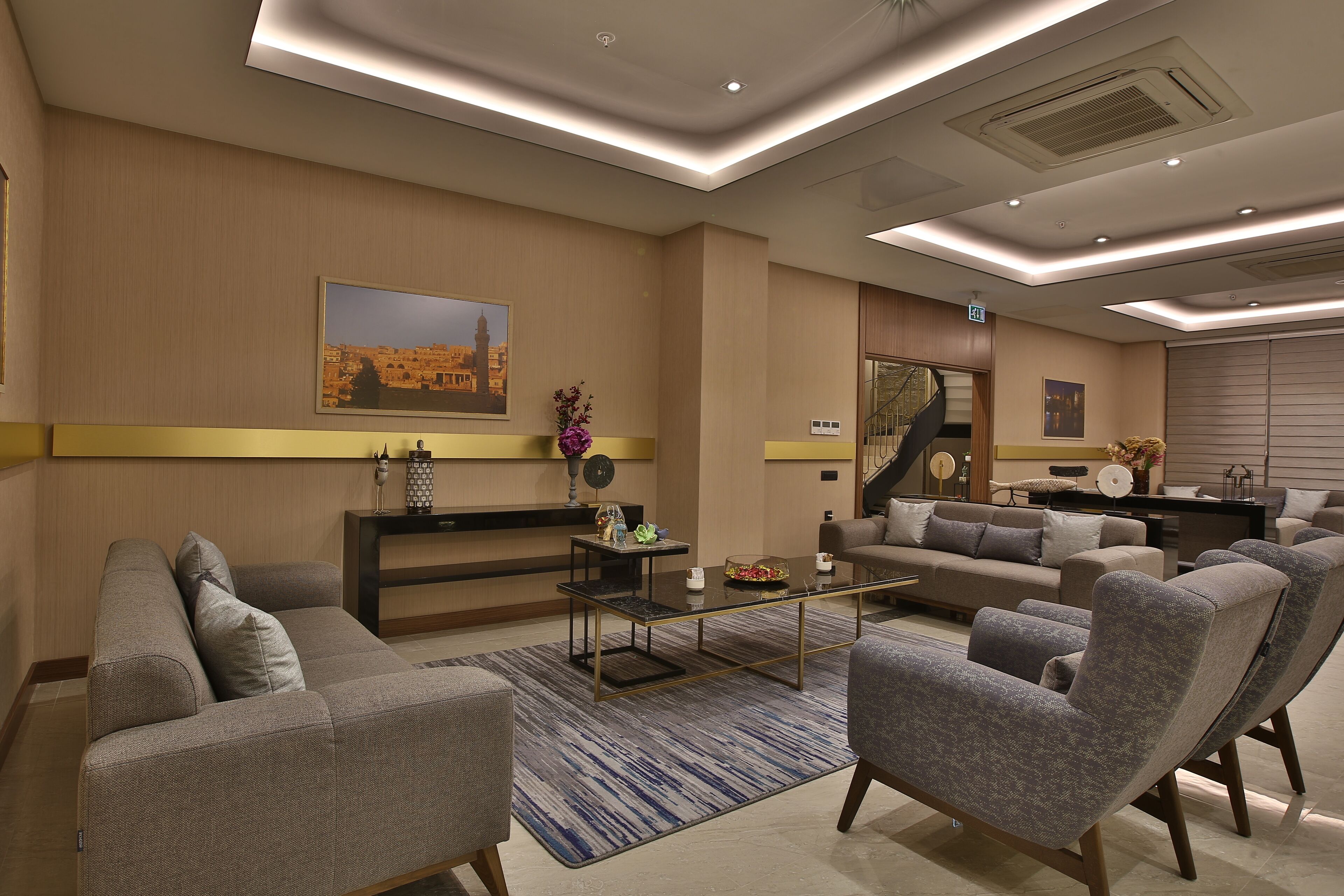 A modern hotel lobby with a sofa, armchairs, a coffee table, and a painting on the wall.