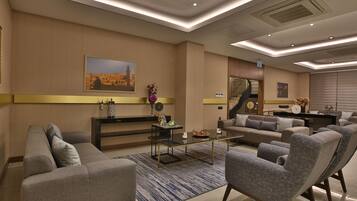 A modern hotel lobby with a sofa, armchairs, a coffee table, and a painting on the wall.