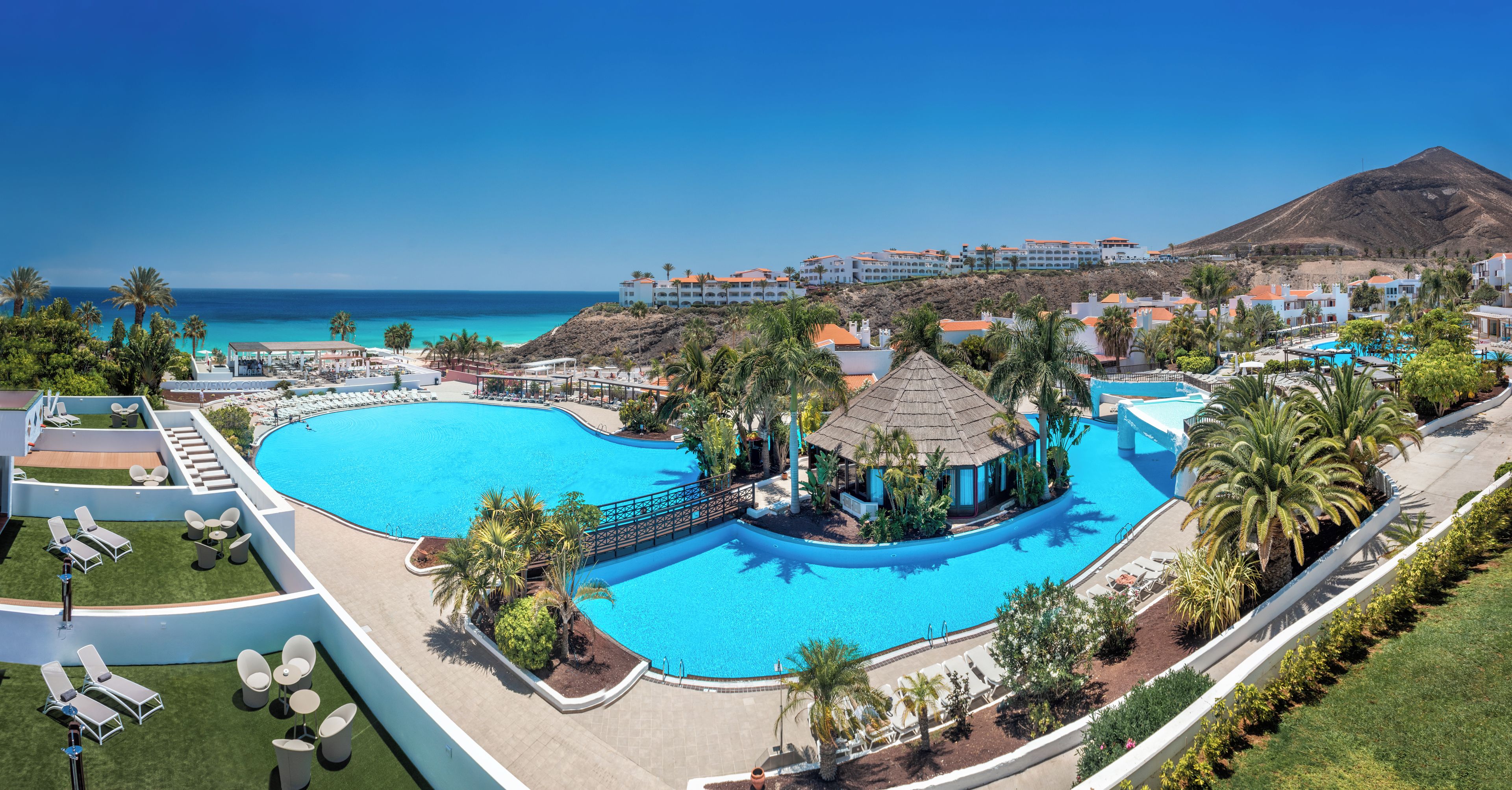 Un resort con una amplia piscina, zonas de descanso y vistas al océano.