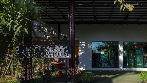 A modern hotel entrance with a signboard, outdoor seating, and a glass facade. - At Border (Aranyaprathet)