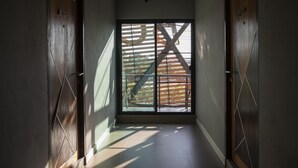 A narrow hallway with wooden doors and a large window with a view of a wooden structure outside. - At Border (Aranyaprathet)