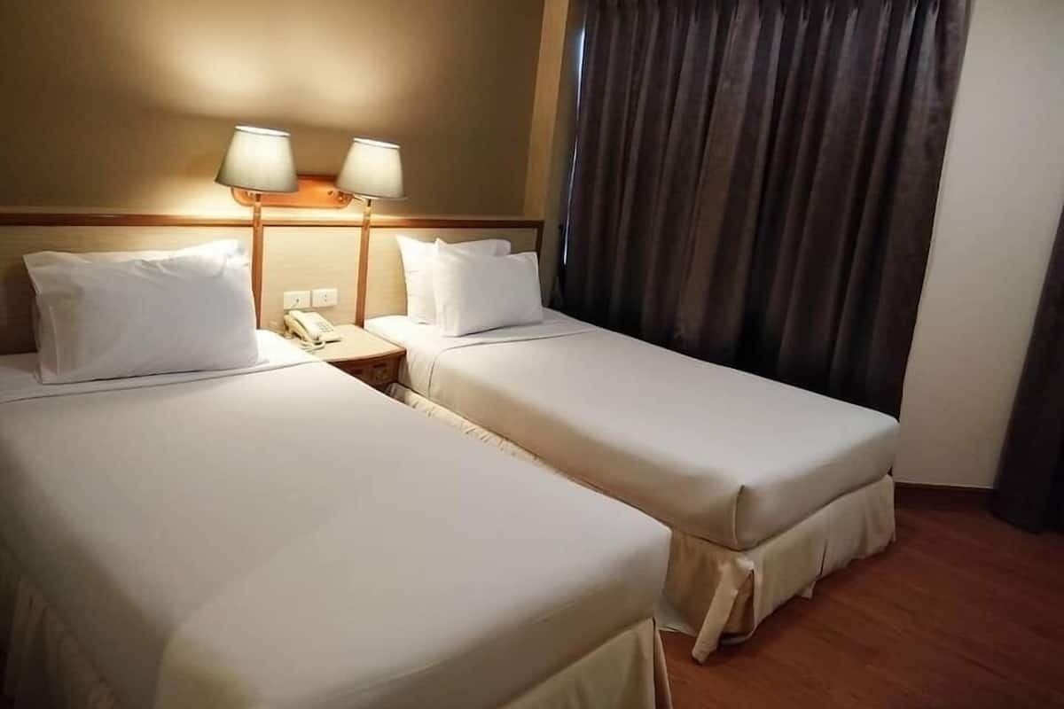 Une chambre d’hôtel avec deux lits, une table de chevet avec une lampe et un rideau.