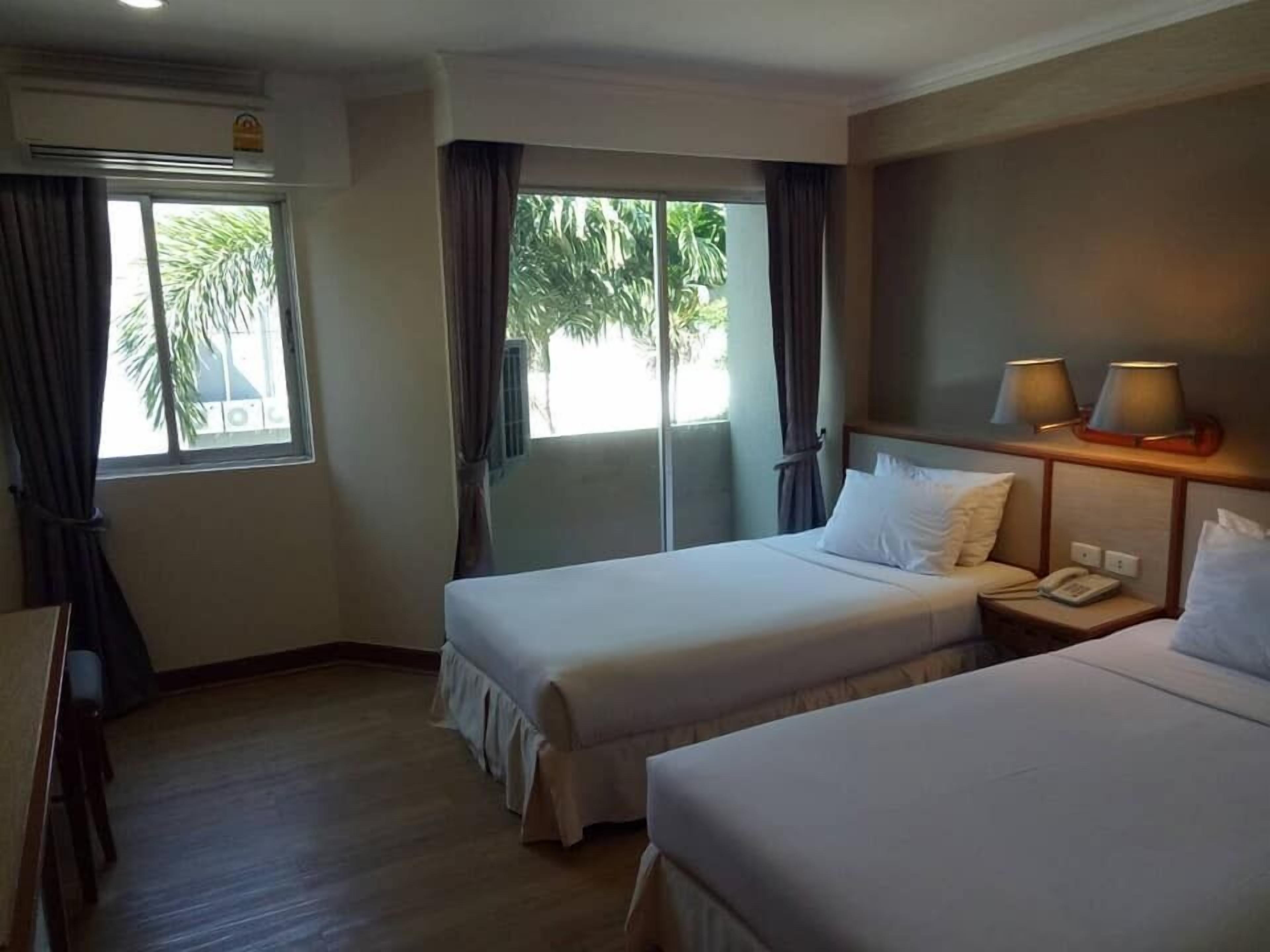 Ein Hotelzimmer mit zwei Betten, einem kleinen Tisch mit Telefon und einem Fenster mit Vorhängen.