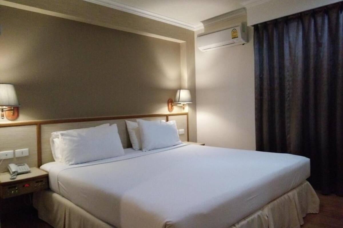 Une chambre d’hôtel avec un grand lit, deux lampes de chevet, un appareil de climatisation et une fenêtre avec des rideaux.