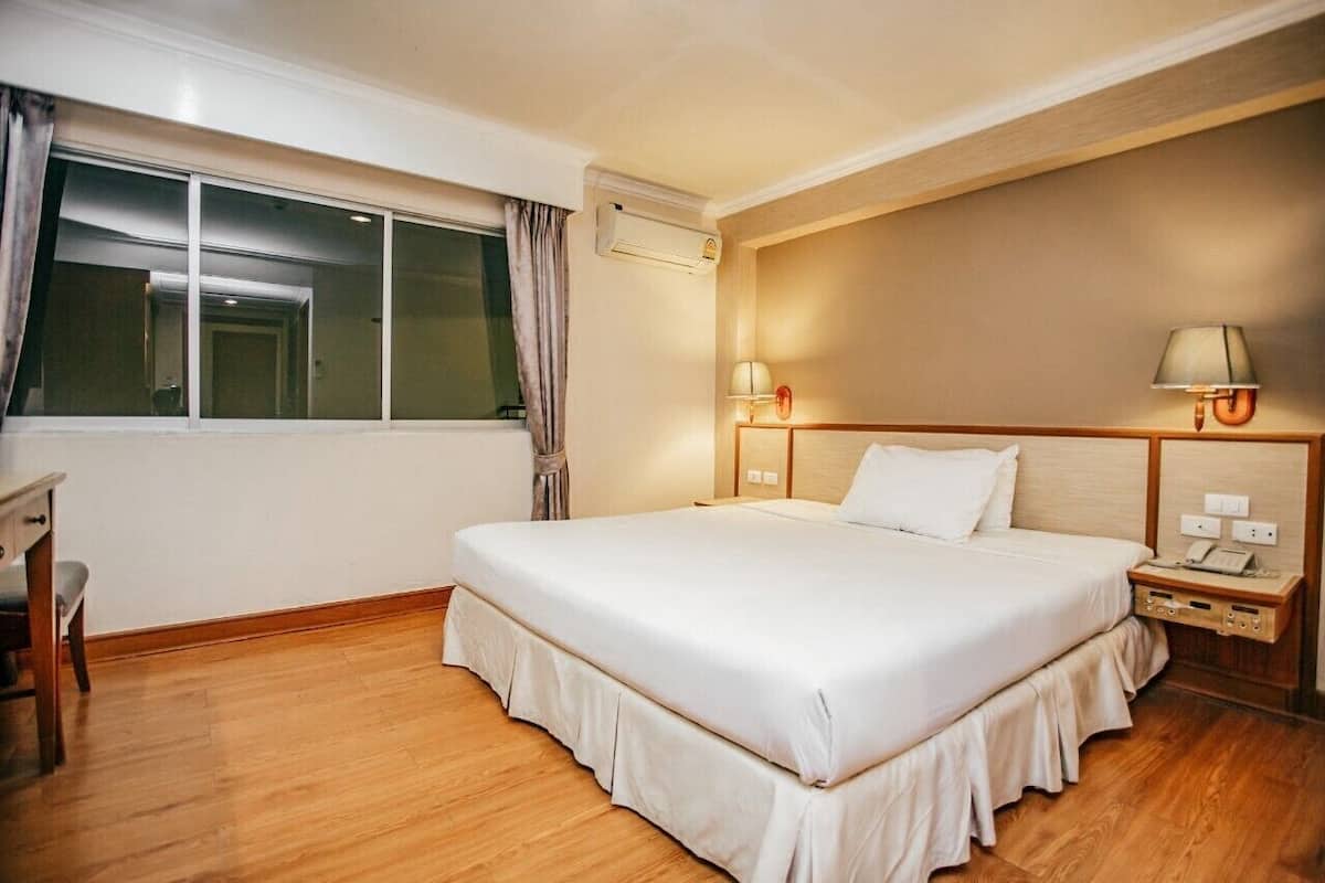 Une chambre d’hôtel avec un grand lit, des lampes de chevet, un bureau et une fenêtre avec des rideaux.
