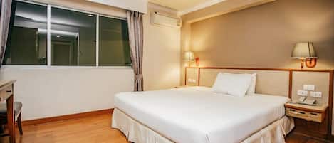 Habitación de hotel con una cama grande, lámparas de noche, un escritorio y una ventana con cortinas.