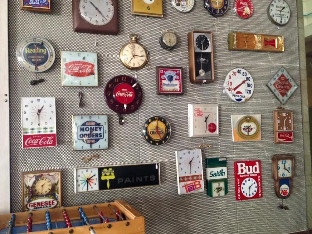 A wall with various clocks and brand logos, including Coca-Cola and Budweiser.