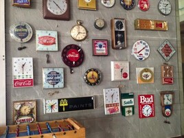 Una pared con varios relojes y logotipos de marcas, incluyendo Coca-Cola y Budweiser.