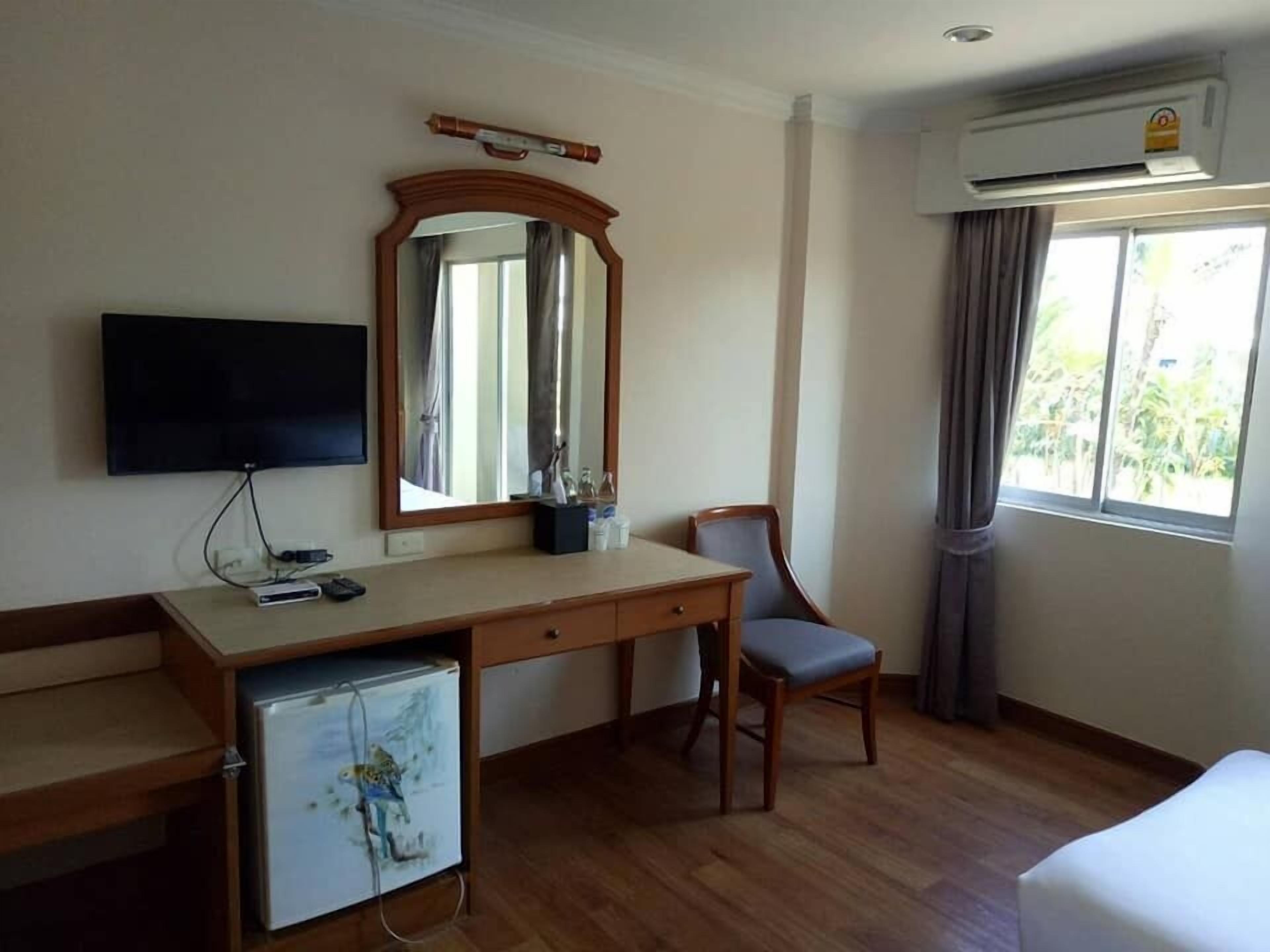 A hotel room with a wooden desk, a chair, a television, a small refrigerator, and a window with curtains.