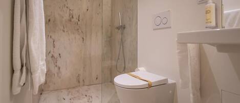 Une salle de bain moderne avec une douche à parois de verre, des toilettes avec une serviette posée sur le siège et un lavabo avec un flacon de lotion.