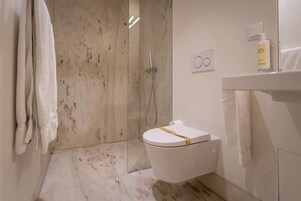 Uma casa de banho moderna com chuveiro envolto em vidro, sanita com toalha no assento e lavatório com frasco de loção.