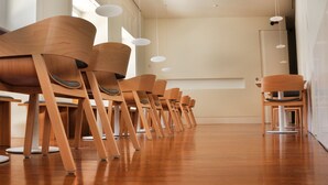 Filea di sedie in legno con sedili e schienali imbottiti, disposte in un ambiente interno moderno con pavimento in legno e lampade pendenti bianche.