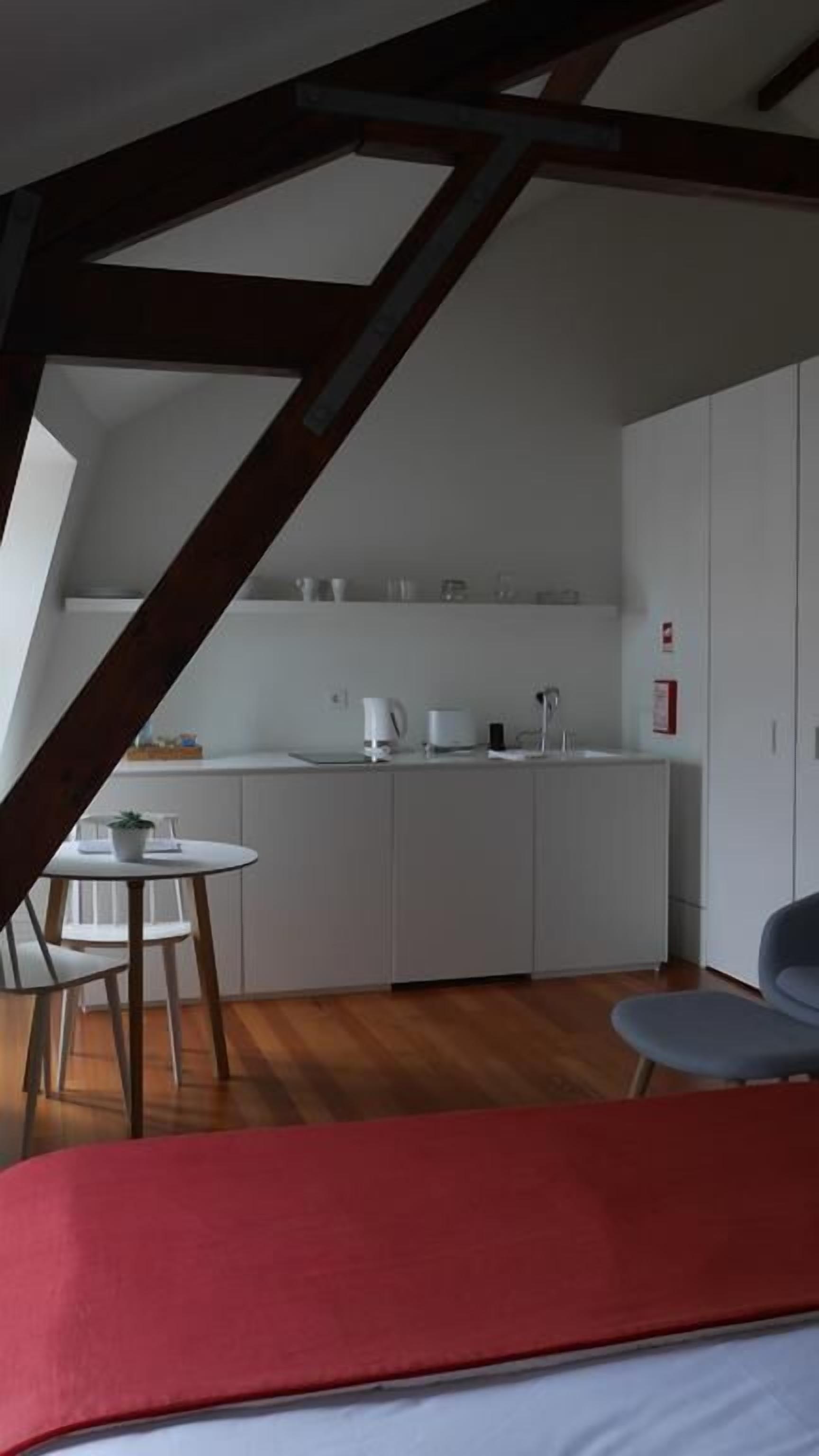 A compact kitchen with white cabinets, a small dining table, and a red bed in the foreground.
