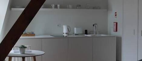A compact kitchen with white cabinets, a small dining table, and a red bed in the foreground.