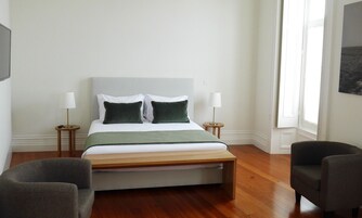 Un dormitorio con cama, dos mesitas de noche, dos lámparas, un banco y dos sillas.
