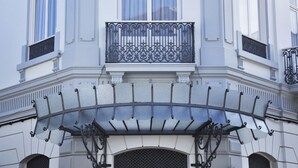 Facciata di un edificio con un balcone caratterizzato da elaborate ringhiere in ferro battuto e un tendaggio decorativo.