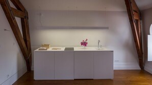 Una cucina moderna con mobili bianchi, soffitto in legno e un piccolo bancone con un vaso di fiori.