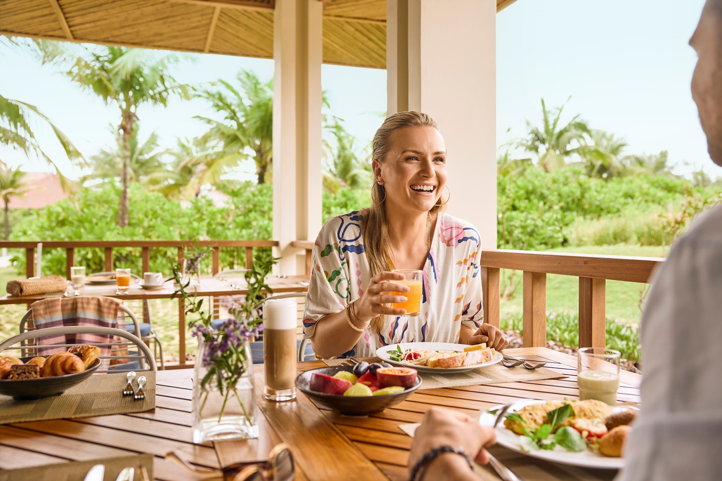A wooden table with breakfast items, a glass of orange juice, and a bowl of fruit.