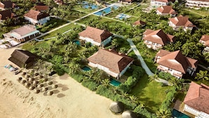 Vue aérienne d’un complexe hôtelier comprenant plusieurs villas, une piscine centrale et une plage.