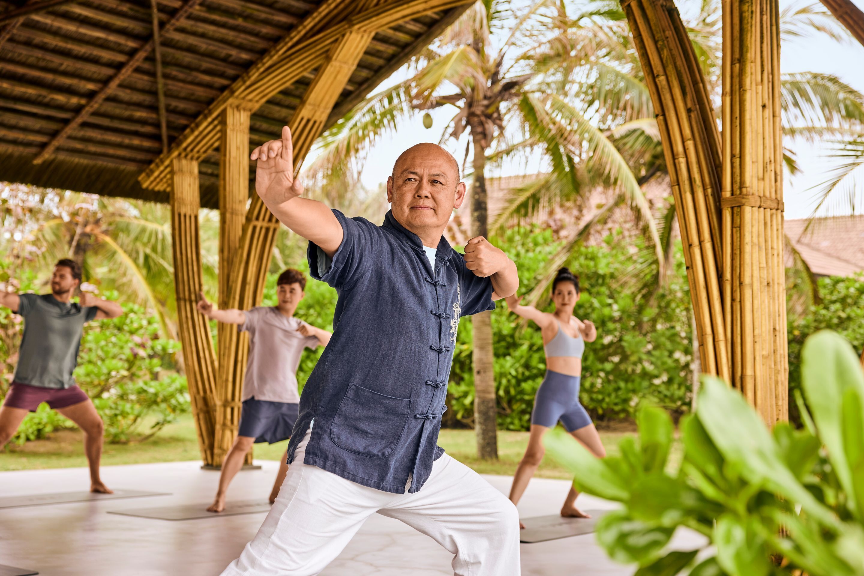 A group of people practicing martial arts outdoors under a bamboo structure.