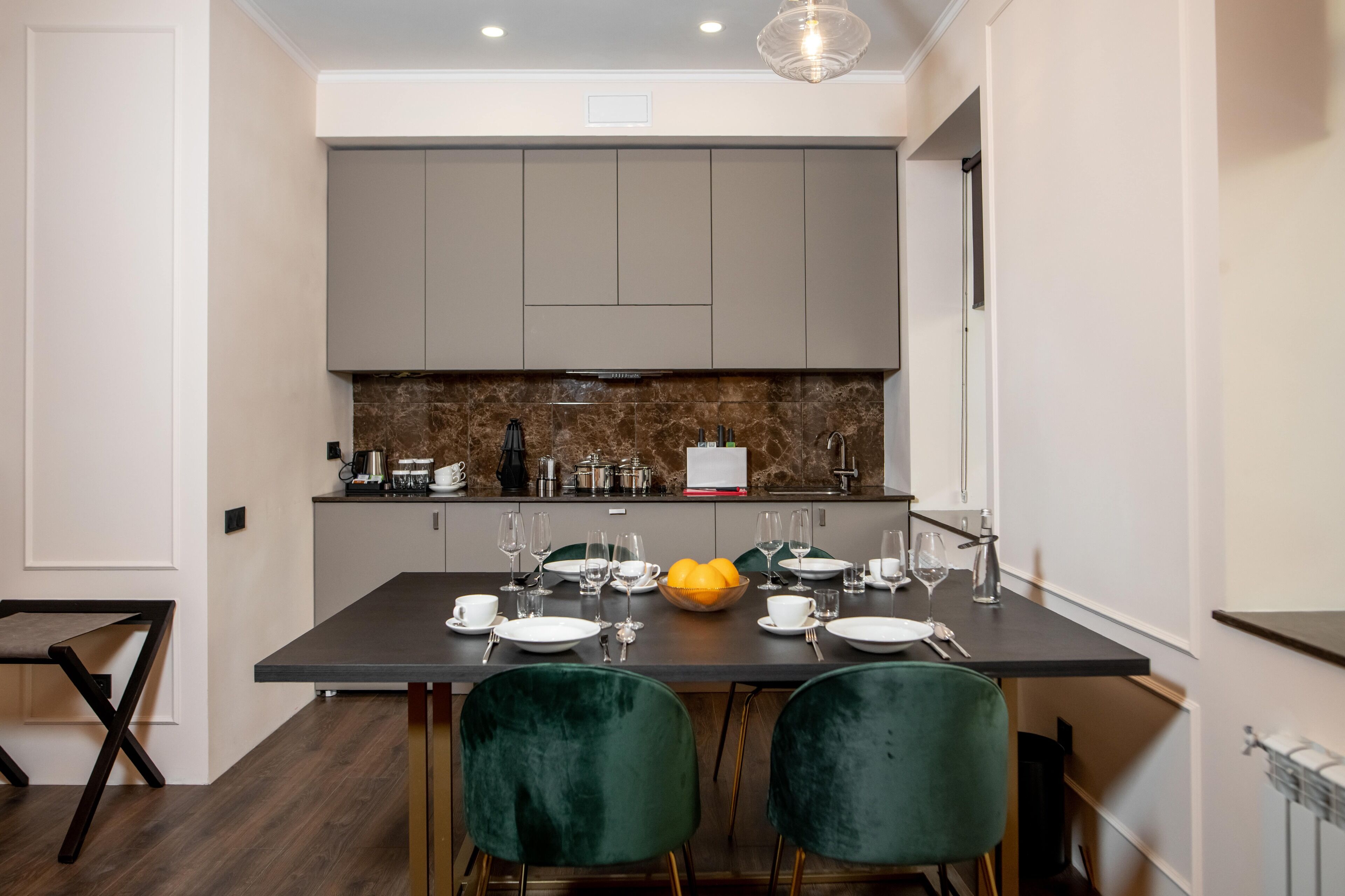 Cocina moderna con armarios grises, salpicadero de mármol y un comedor con dos sillas verdes y una mesa dispuesta para cuatro.
