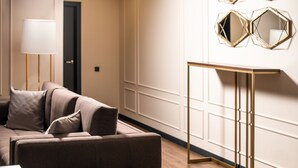 A modern living room with a brown sofa, a standing lamp, and a gold-framed console table against a white wall with paneling. - De Paris Apartments (Kyiv)