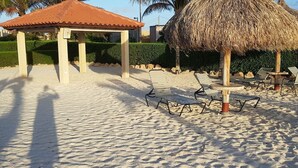 Une zone de plage avec un parasol en chaume, des chaises longues et un kiosque.