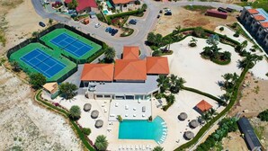 Vue aérienne d’un complexe hôtelier doté d’une piscine, de courts de tennis et d’un grand bâtiment surmonté d’un toit rouge.