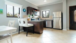 Une cuisine moderne dotée d’un îlot central, d’un coin repas avec une table et des chaises blanches, et d’un réfrigérateur.