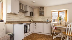 Una cucina compatta con mobili bianchi, un piano di lavoro in legno, forno integrato e un'area pranzo con tavolo e sedie.