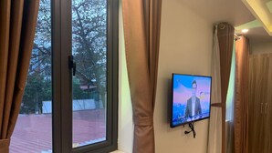 Een kamer met een aan de muur bevestigde televisie, een raam met gordijnen, een houten stoel en een houten deur.