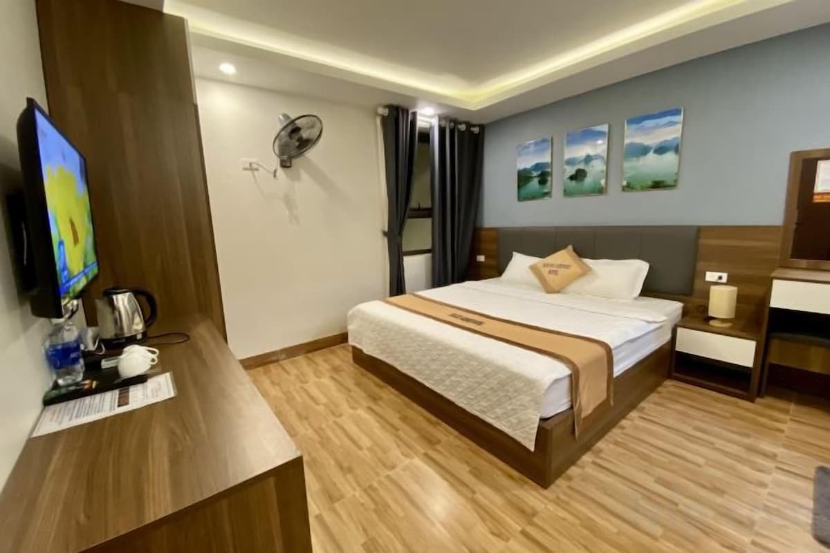 Una habitación de hotel con cama, mesita de noche y escritorio con computadora.